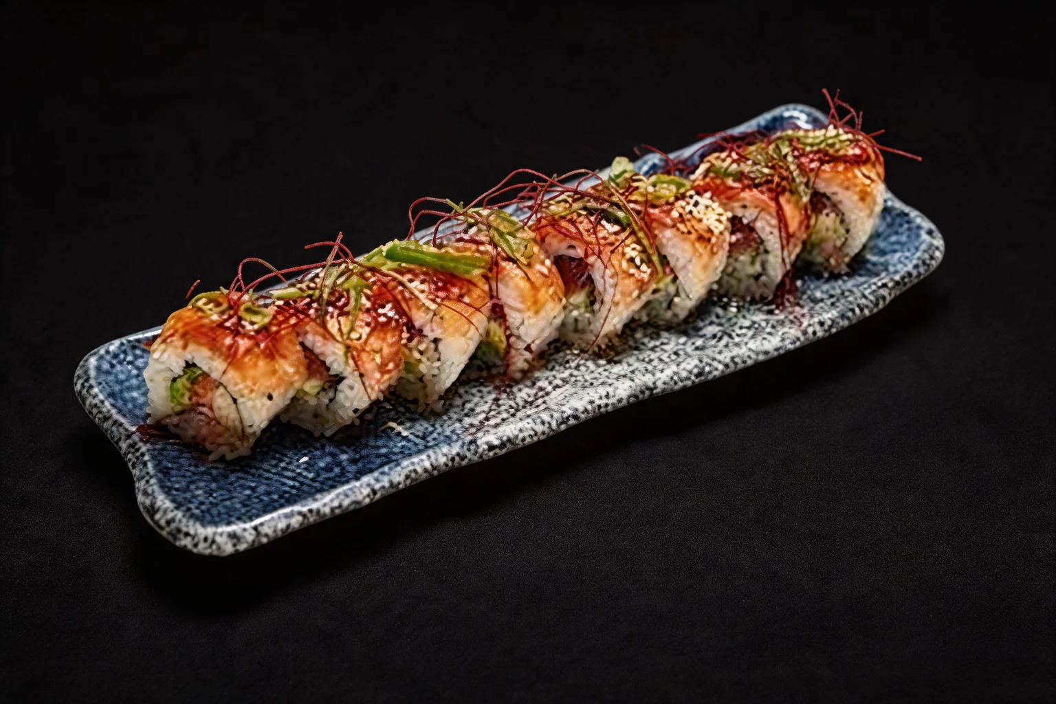 Signature saumon Roll sur un plat long bleu moucheté, fond sombre.