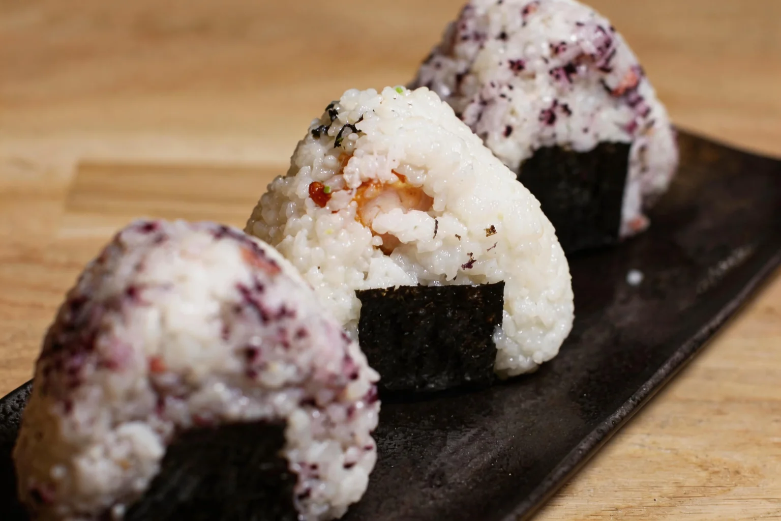 Onigiri sur un plat long noir, table en bois.